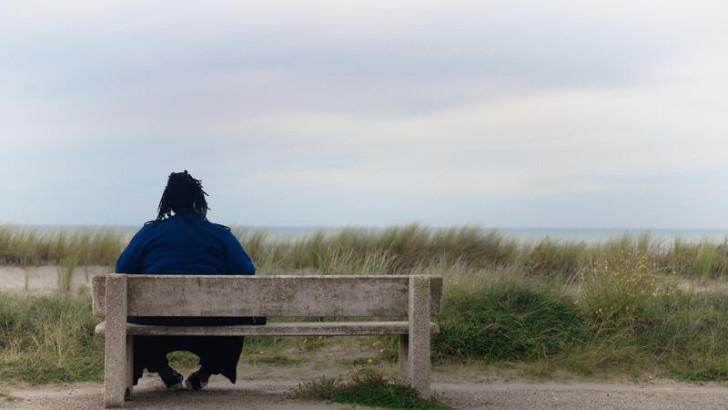 De dos, Nelda, assise sur un banc, regarde la mer